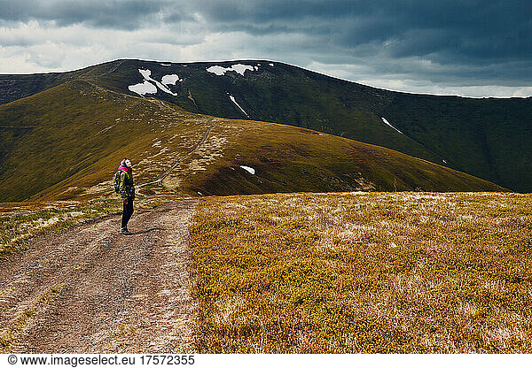 A woman walks along a mountain path along a mountain range.