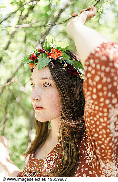 A woman with a flower crown grabbing a tree branch