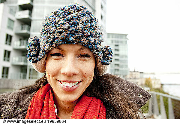 A woman with a warm blue hat  and red scarf smiles at the camera.