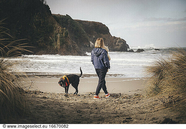 A woman with an infant is playing with a dog on the Californian beach