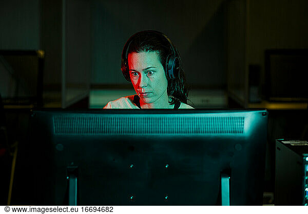 A woman with an intense gaze works at desktop computer in dark room