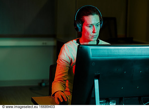 A woman with computer mouse in hand works at computer in dark room