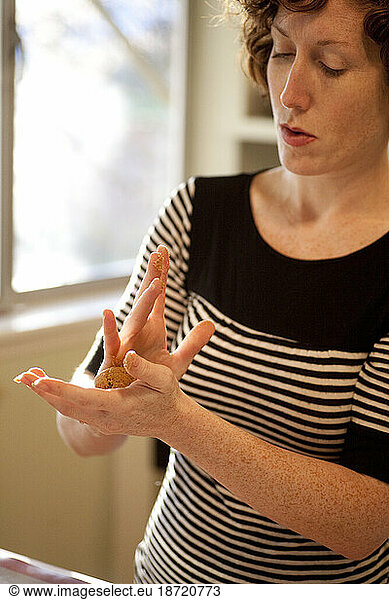 A woman with freckles molds dough into balls for Christmas cookies in Seattle  Washington.