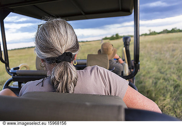 A woman with grey hair seated in a safari vehicle  obserrving wildlife
