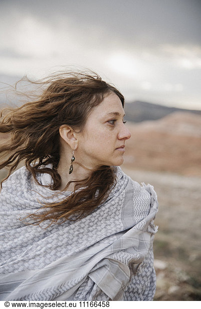 A woman with long hair blowing in the wind standing in a desert landscape.