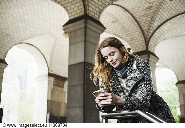 A woman with long hair looking at her smart phone  under an archway.