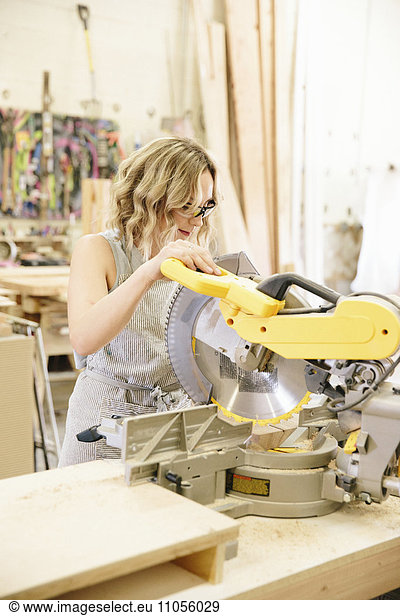 A woman woodworker using a mechanical saw to cut wood on a workbench.