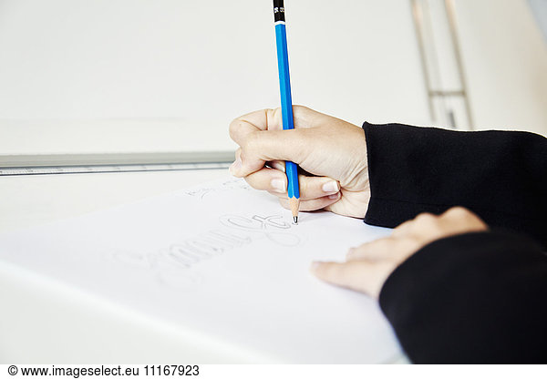 A woman working on a graphic on a drawing board  outlining letters with a pencil.