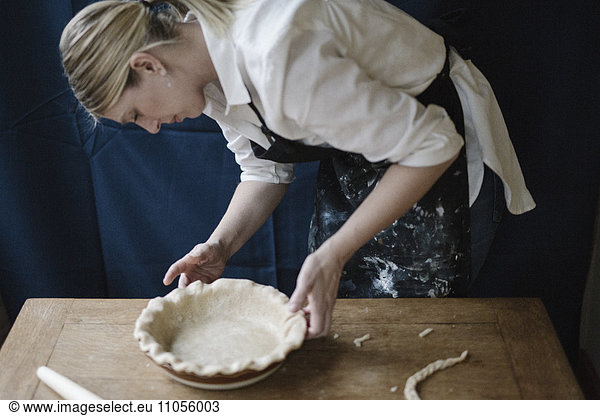 A woman working smoothing the edge of a pastry case lining a pie dish.