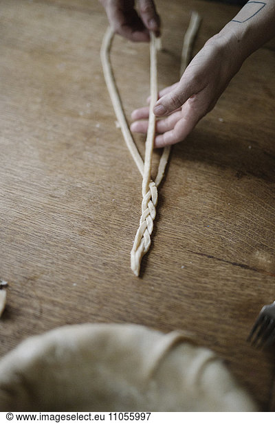 A woman working with raw pastry  plaiting three strands of dough.