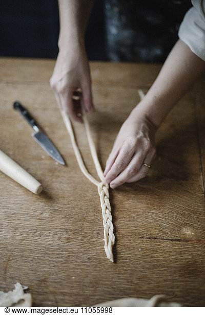 A woman working with raw pastry  plaiting three strands of dough.