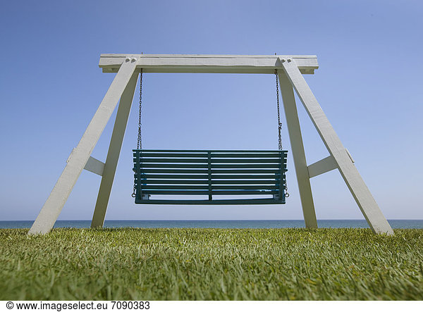 A wooden beach swing with a green painted seat. A good view of the sea.