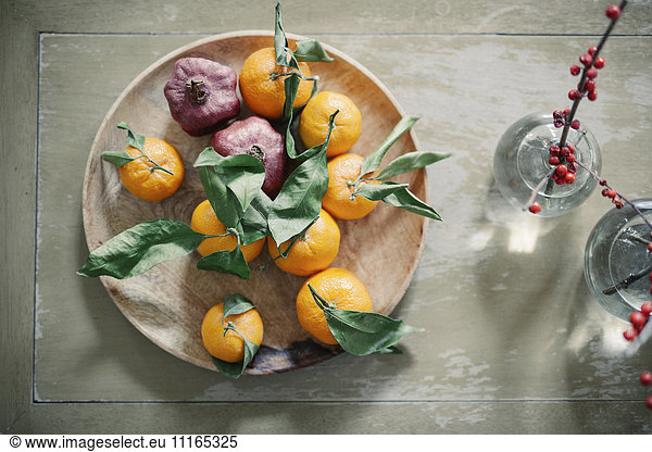 A wooden bowl of oranges  citrus fruits on a table top.