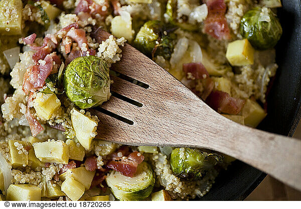 A wooden spatula rests over a pan of organic vegetables  couscous and bacon in a home kitchen in Seattle  Washington.