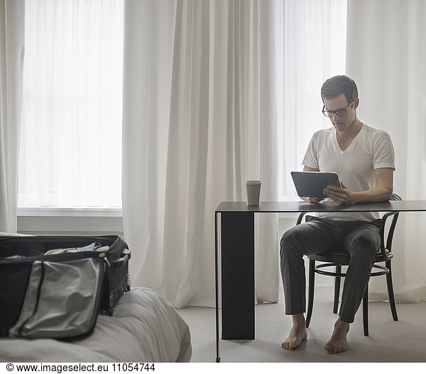 A working day. A man seated at a laptop computer  working in a hotel bedroom.