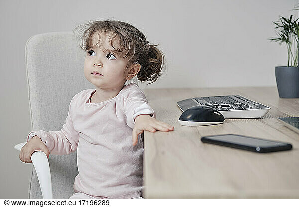 A 2-year-old girl is sitting in an office chair with a keyboard  mouse