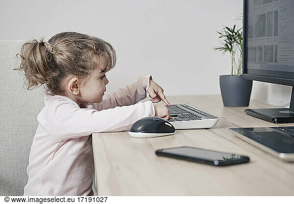 A 2 year old girl is using a computer keyboard while sitting in an office chair