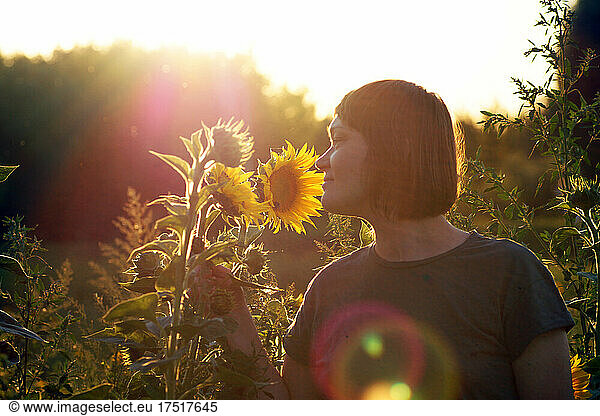 A 40-year-old woman stands in a field of sunflowers at sunset