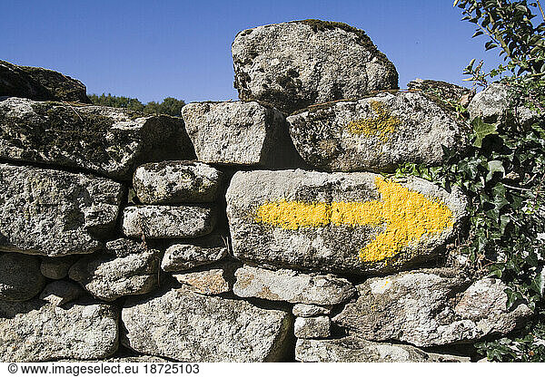 A yellow arrow on an old stone wall points the way to pilgrims walking the Camino de Santiago in Galicia  Spain.