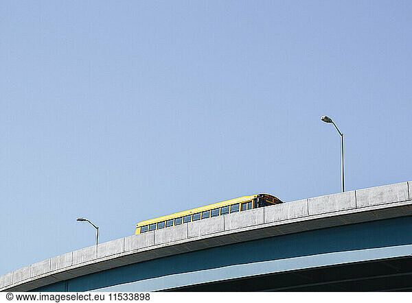 A yellow schoolbus driving over an elevated roadway against a blue sky.