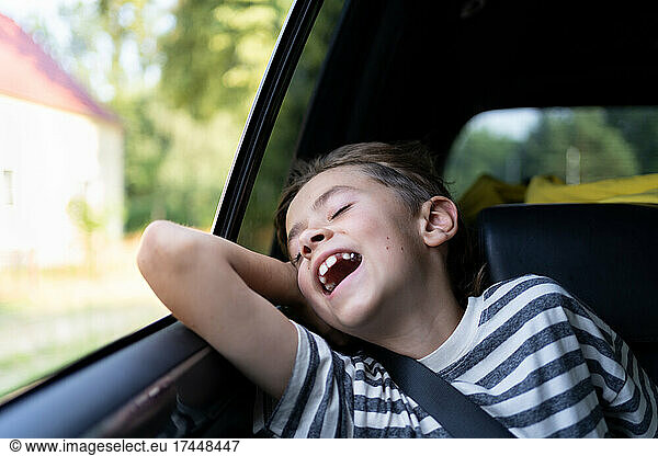 A young boy is enjoys the warm wind from an open car windowdow