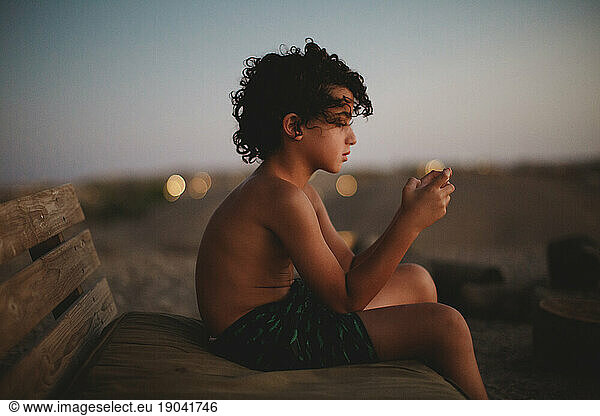A young boy playing with his smartphone in desert during sunset