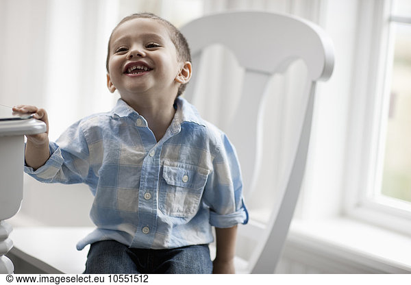 A young boy sitting on a chair  smiling and looking up.