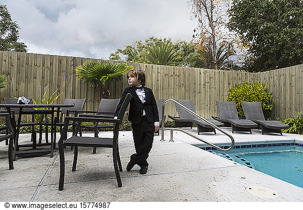 A young boy wearing formal attire standing by pool