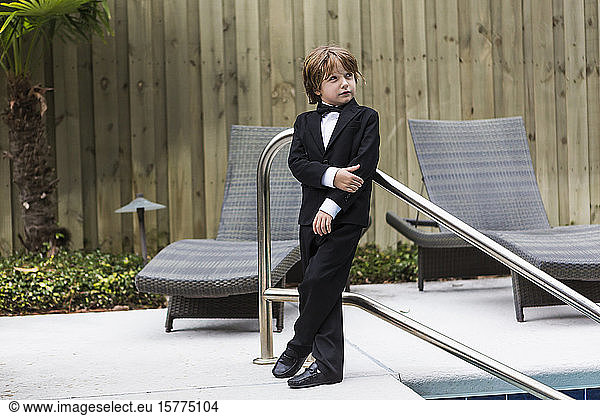 A young boy wearing formal attire standing by pool