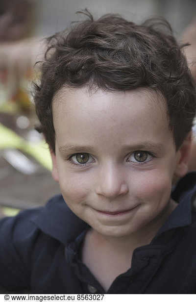 A young boy with dark hair and brown eyes  looking upwards and smiling.
