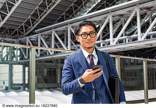 A young businessman in the city  on the move  a man in a blue suit with a laptop bag  holding a mobile phone.