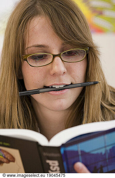 A young caucasian college student chews on her pen while studying.