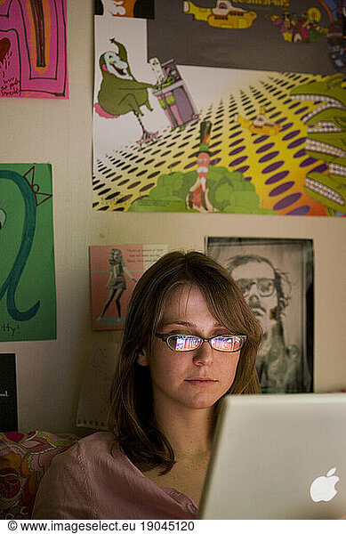 A young caucasian college student works on her laptop while sitting in her dorm room.
