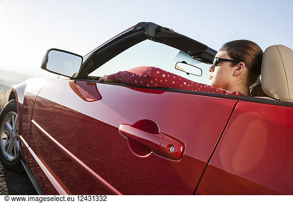 A young Caucasian woman in a convertible sports car.