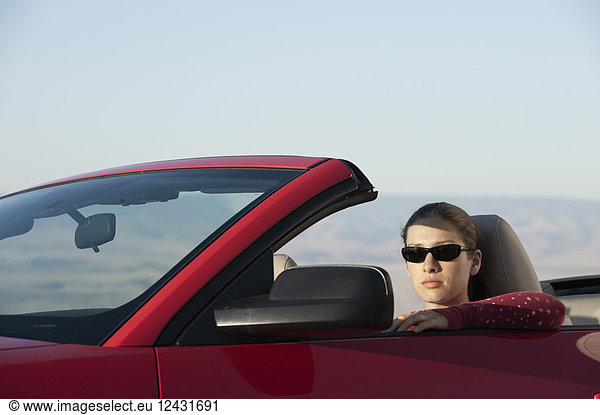 A young Caucasian woman in a convertible sports car.