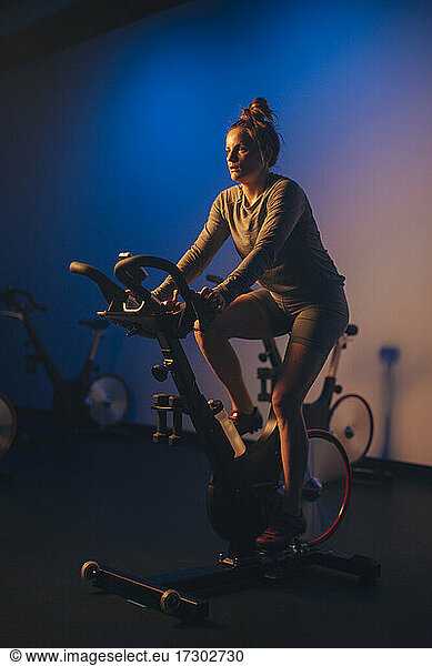 A young Caucasian woman pedals a stationary bike in an indoor studio.