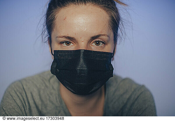 A young Caucasian woman pedals in an indoor studio with a mask.