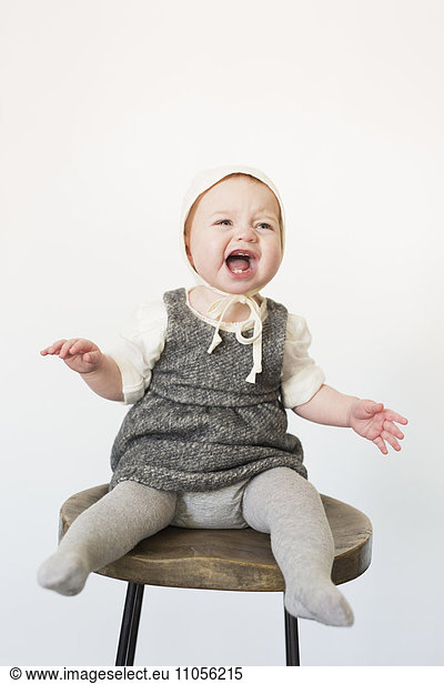 A young child  a girl sitting on a tall stool laughing.
