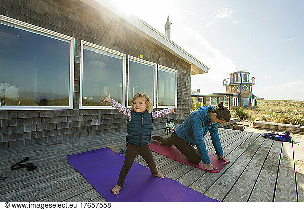 A young child does yoga on a deck with her mother
