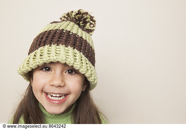 A young child with long brown hair  wearing a knitted hat with a pompom.