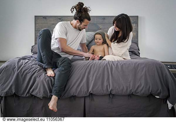A young couple and their young son sitting together on their bed.