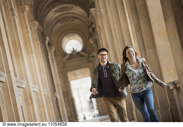 A young couple walking down a colonnade in the historic heart of a city.