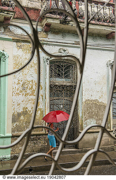 A Young Cuban Woman Walks Through the Rain Holding a Red Umbrella. Santa Clara  Cuba
