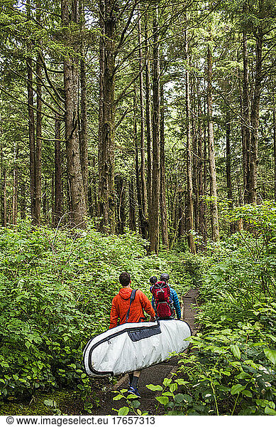 A young family walks down forested path with surfboard