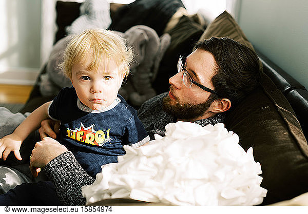 A young father cuddling with his son on the couch.