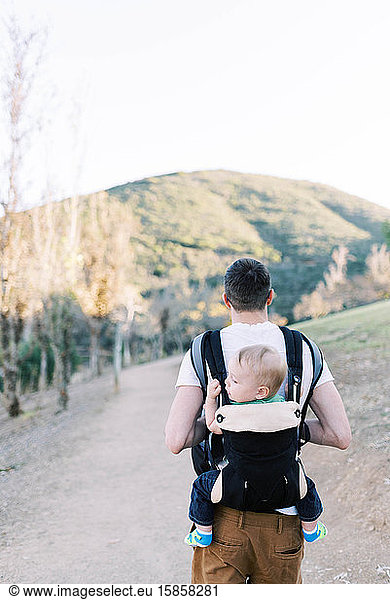 A young father hiking while carrying his son on his back.