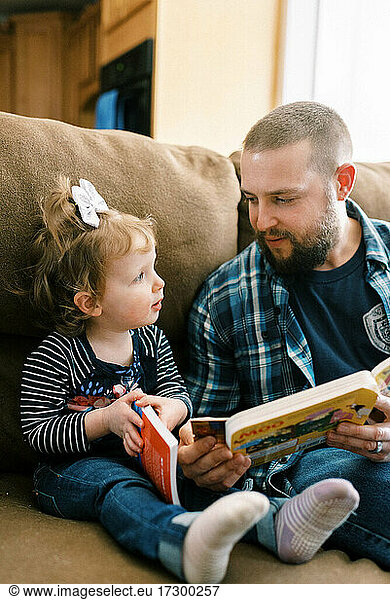 A young father interacting with his daughter and reading together