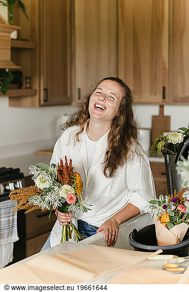 A young female farmer standing in her kitchen holding a bouquet