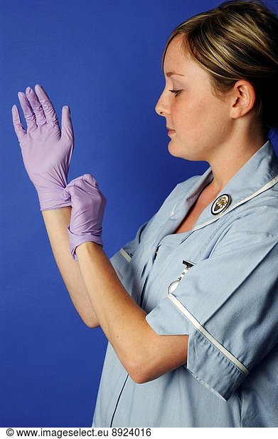 A young female nurse putting on a pair of latex gloves. Gloves are worn throughout medicine and science  to prevent cross contamination.