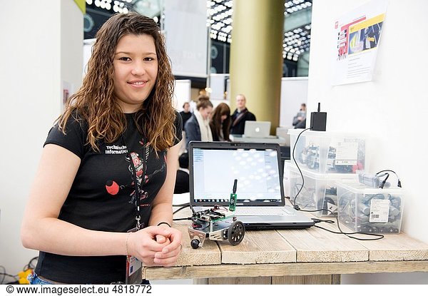 A young female student demonstrate her robot guides by a computer